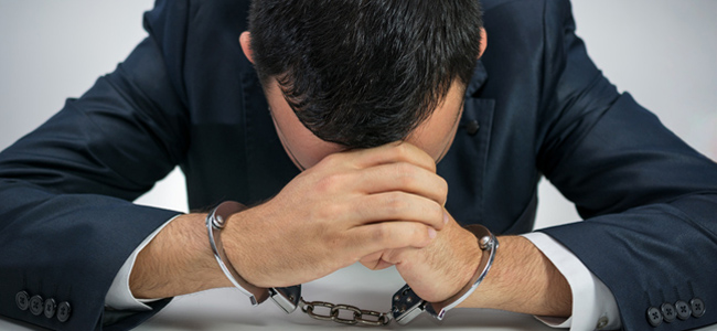 white young businessman handcuffed. he is sitting at a table wit